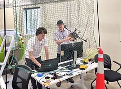 A person in a lab working on a computer and holding a drone.