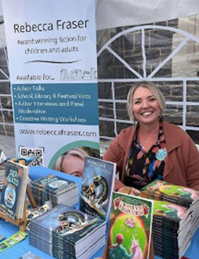 Rebecca Fraser at a table with several piles of her books.