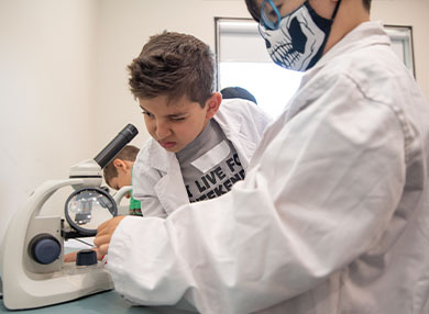 Two children in lab coats looking at a microscope.