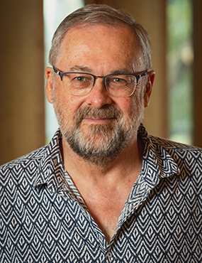 Geoff Mackellar, a smiling, bearded man in glasses and a patterned blue and white shirt.