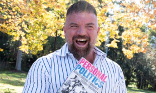 Associate Professor Leigh Boucher smiling and holding his book, 'Personal Politics'