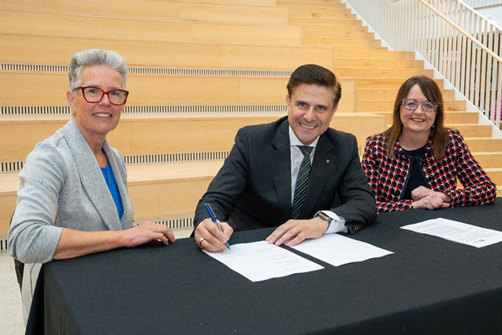 Professor Talal Yassine AM and two other people sitting at a table signing a document.