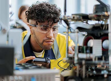 A person in a lab holding a controller and looking at electronics.