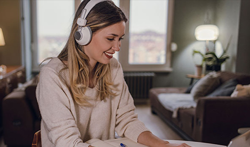 Women in pink jumper studying online on her laptop with headphones on her head