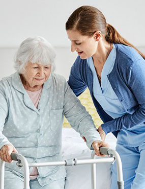 An aged care worker helping a person with a walker.