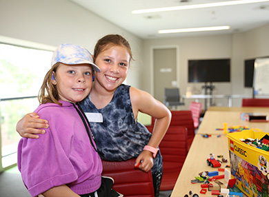 Two students smiling at the camera next to a table of Lego and toys.