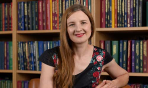 A person sitting and smiling in front of bookcases filled with books.