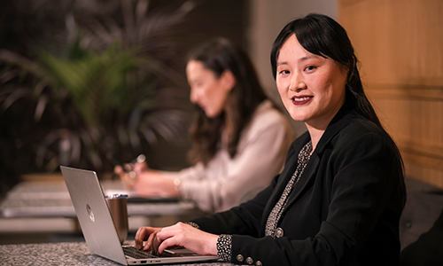 Lady typing on a laptop looking and smiling directly at the camera