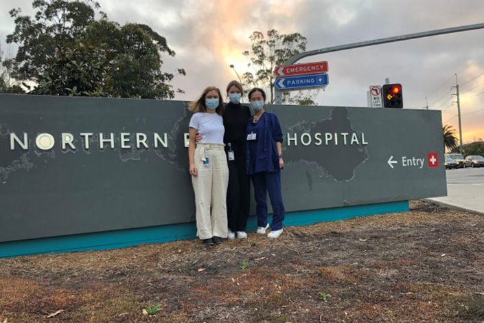 Jordan with colleagues wearing facemasks in front of the Northern Beaches Hospital signage