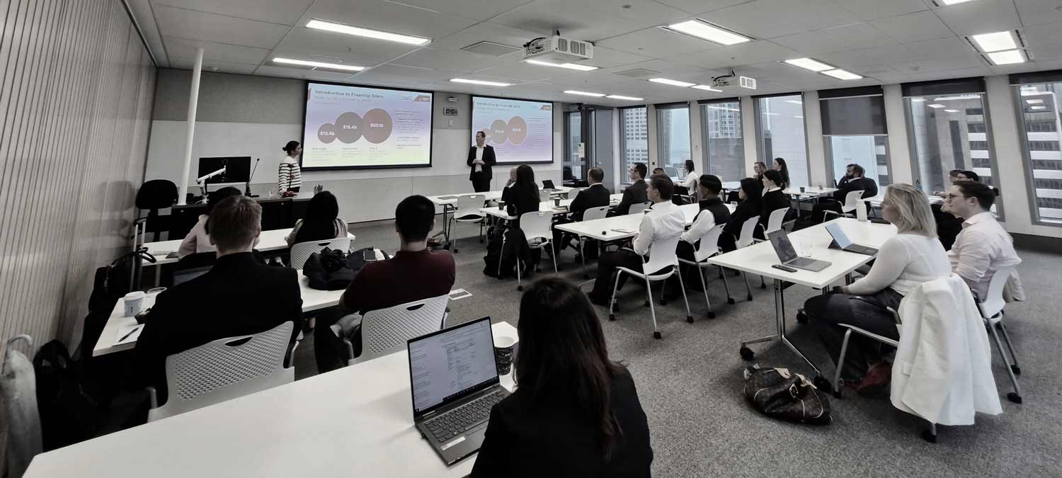 A seminar room full of seated people looking at screens with charts on them.