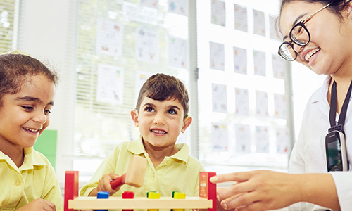 Two children play with blocks at a table with a medical student in a lab coat.