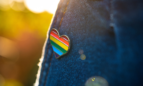 A heart-shaped pride flag pin on a denim jacket.