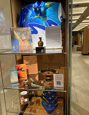 A museum display case containing numerous objects relating to the ancient and modern Olympic Games