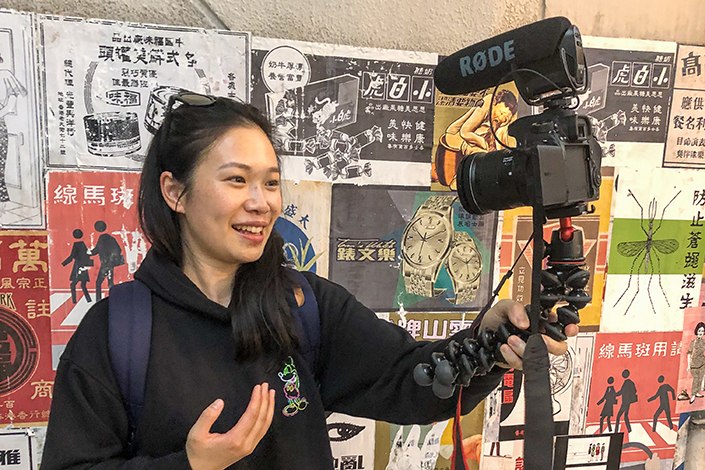 Janice Fung Vlogging infront of a poster covered wall