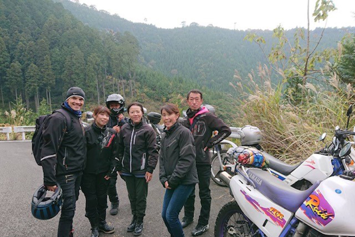 Josh Kidd with his wife, a group of people and motorbikes, on a winding hilled road