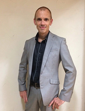 Josh Kidd posing for a photo in a silver suit and black butoned up shirt