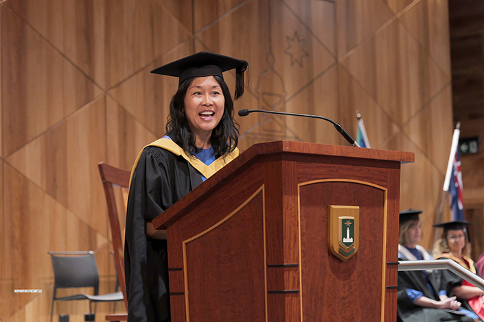 Kathrina Lo speaking at a graduation ceremony on stage into a microphone