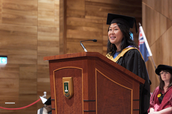 Kathrina Lo speaking at a graduation ceremony on stage into a microphone