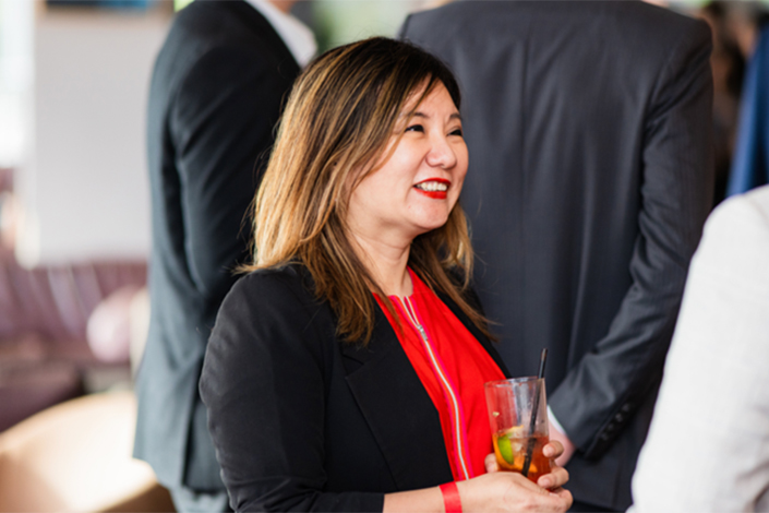 Lady in a red shirt and black blazer smiling while listening at the Beer with a Boss event